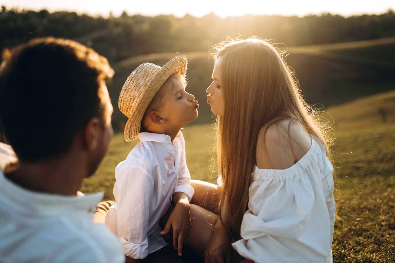 Une mère et son enfant, front contre front, dans les herbes au soleil couchant.